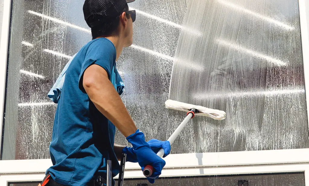 male professional cleaning service worker in overalls cleans the windows and shop windows of a store with special equipment
